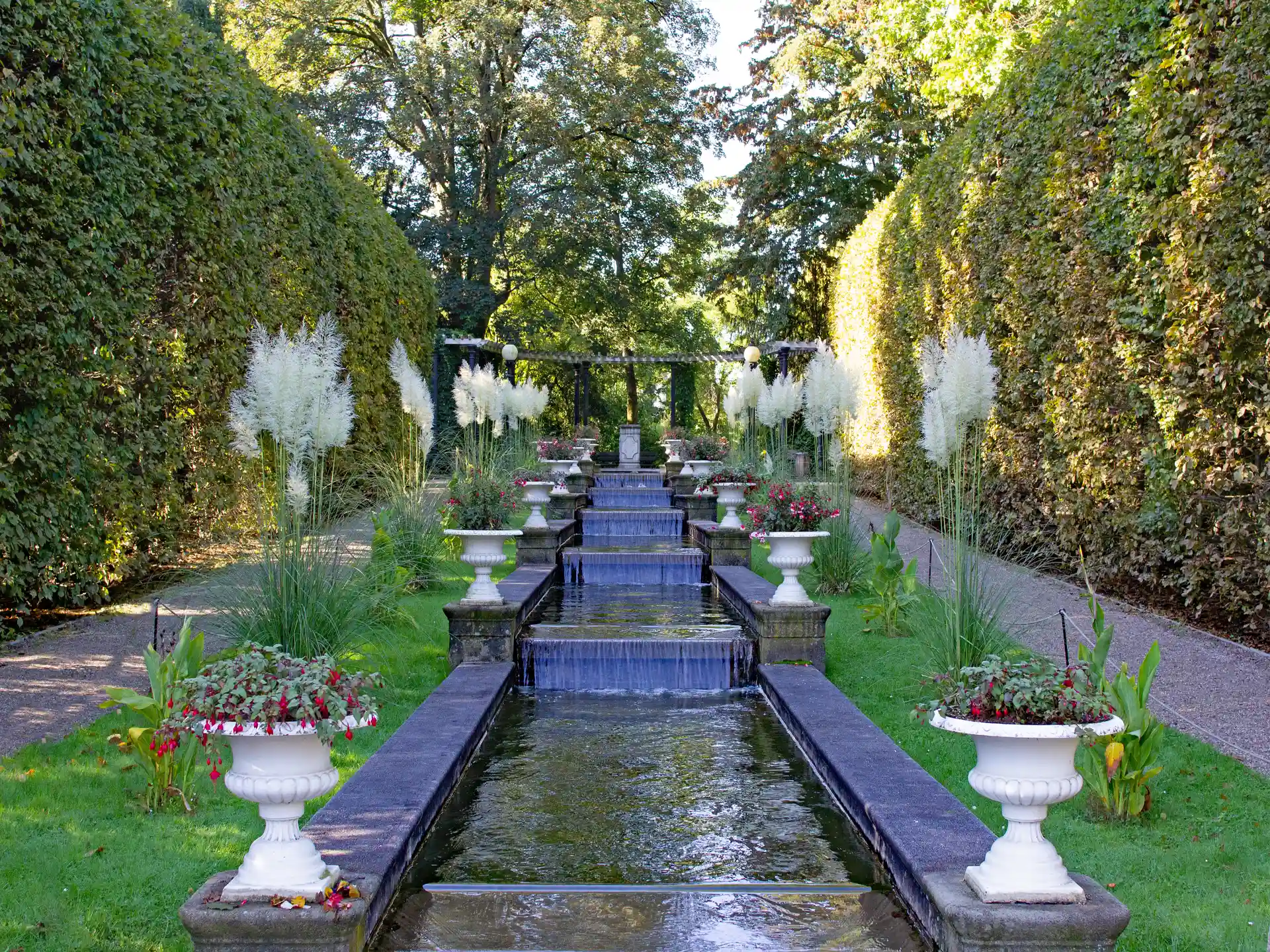 Formale Gartenanlage mit Wasserachse mit Pflanzkübeln und Pampasgras am Wegesrand.