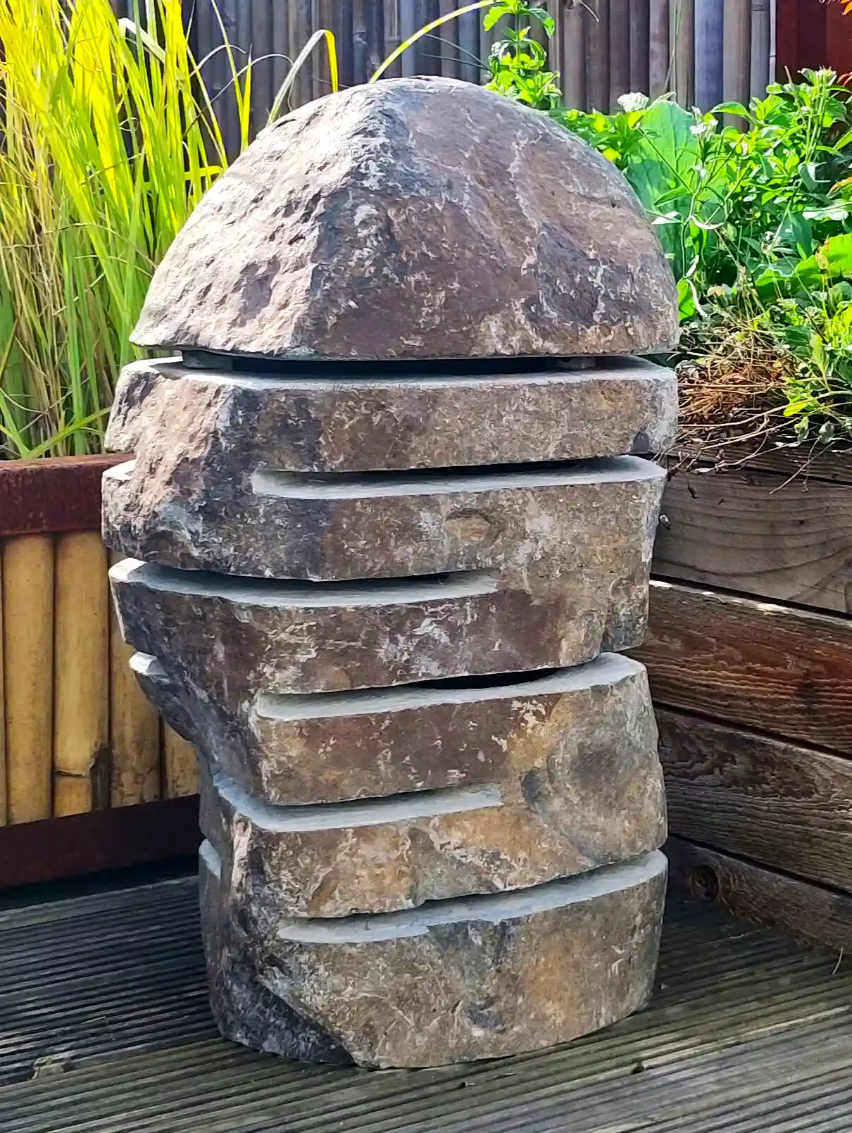 Steinlampe aus indonesischem Flussstein Steinlampe mit warmen Licht neben Blumenbeet und Holzeinfassung im Garten.