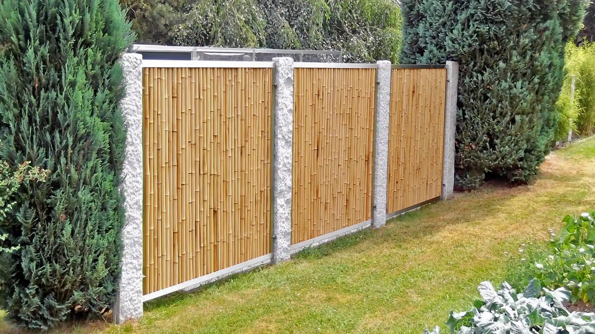 Bambuszaunfelder mit Metallrahmen und Pfosten als Sichtschutz in einem bepflanzten Garten.