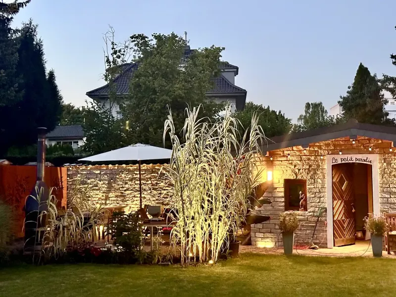 Buntes Pfahlrohr Arundo donax 'Variegata' neben einer Terrasse und Steinmauer